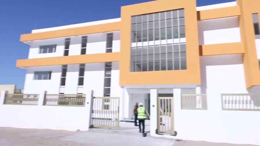 Ghernata school building: two-storey white facade with orange bands and a large glazed entrance, site team at the gate